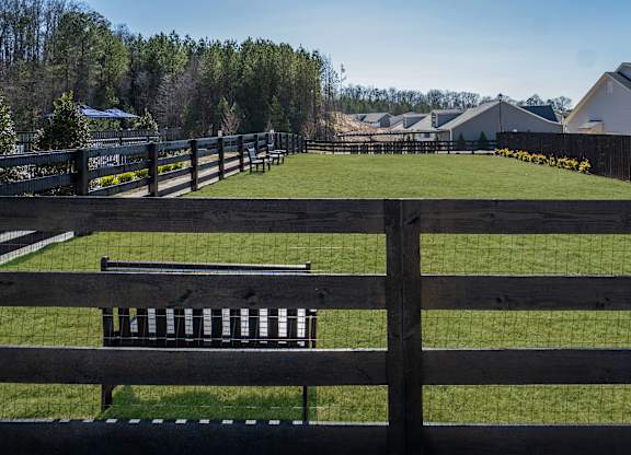 A wooden fence in front of a grassy field with houses in the background.