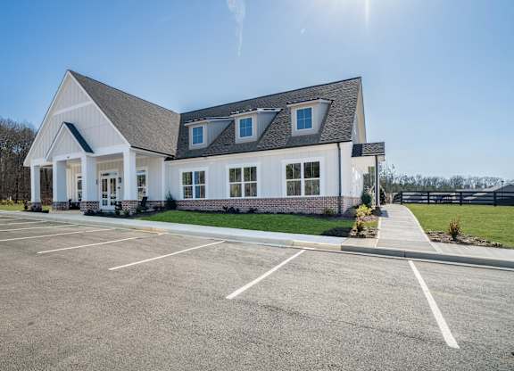 A white building with a grey roof and a parking lot in front.