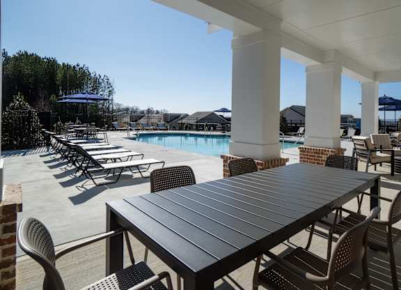 A table and chairs are set up on a patio with a pool in the background.
