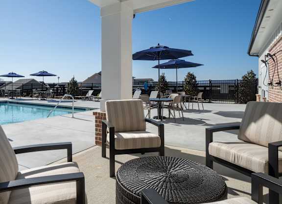 A patio with chairs and a table overlooks a pool.