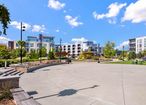 A large open plaza with a flagpole and apartment buildings in the background.
