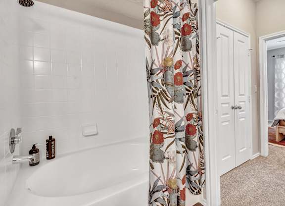 A white bathtub with a shower head and a shower curtain with a floral pattern.