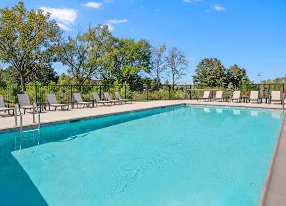 A large swimming pool surrounded by trees and lounge chairs.