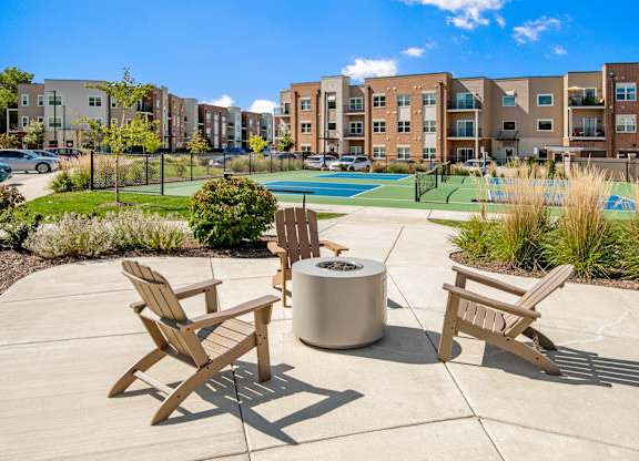 A sunny day at a poolside with chairs and a fire pit.