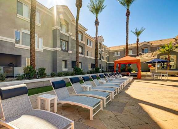 A row of lounge chairs are set up on a patio in front of a building.