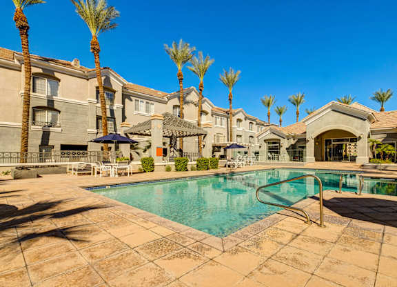 A swimming pool surrounded by palm trees and a building in the background.