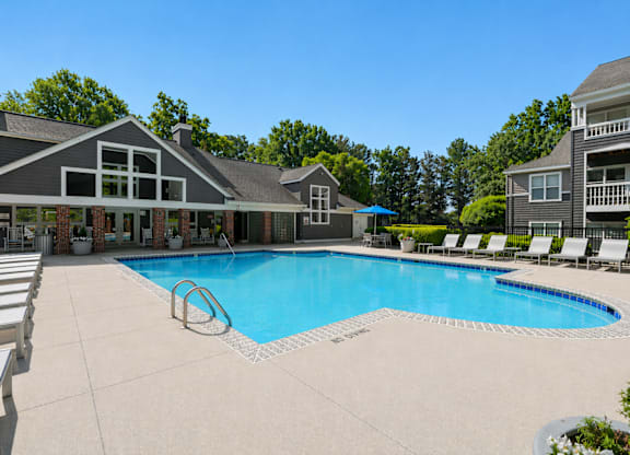 A large swimming pool in front of a house with a deck and lounge chairs.