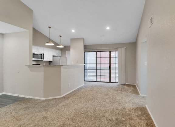 A spacious living room with a kitchen area and a large window.