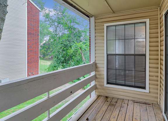 A balcony with a window and a view of a green tree and a red building.