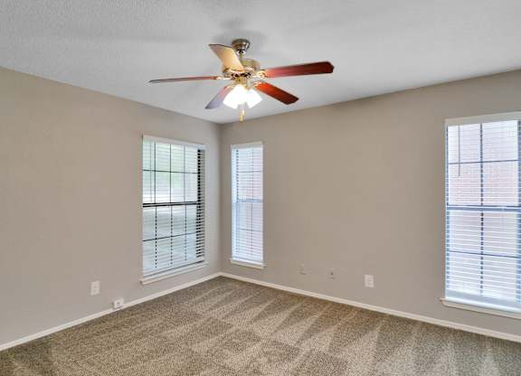 A room with a ceiling fan and two windows.