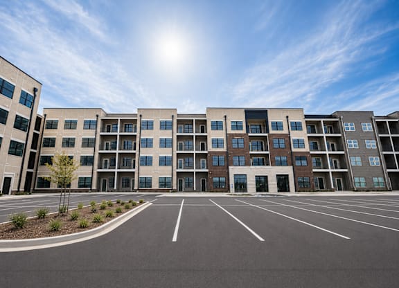 A sunny day at a modern apartment complex with a parking lot in front.