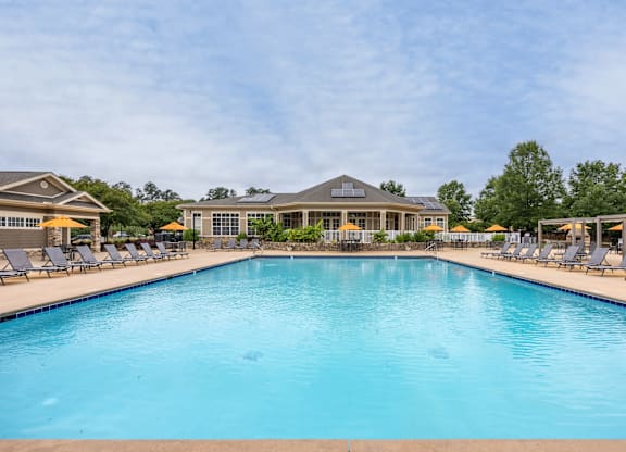 A large swimming pool in front of a building with lounge chairs on either side.