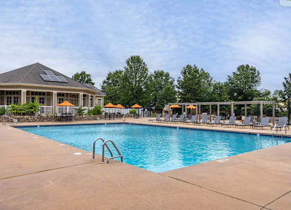 A large outdoor swimming pool with a sun lounger chairs and a building with solar panels on the roof.