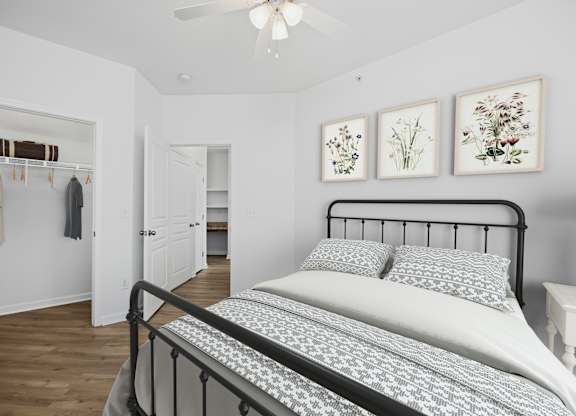 A bedroom with a bed, a ceiling fan, and three framed pictures on the wall.
