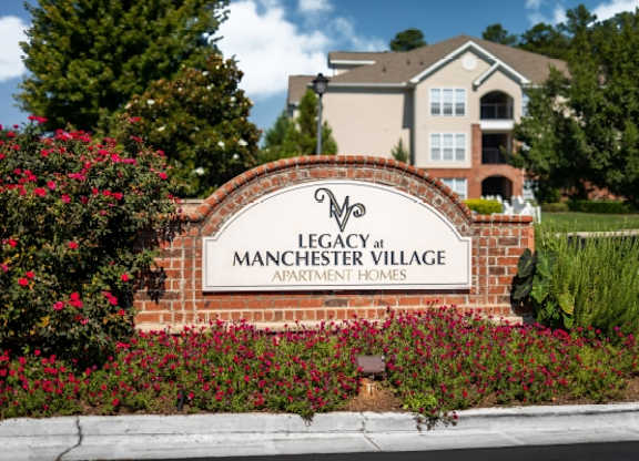 A brick sign that says Legacy at Manchester Village in front of a building.