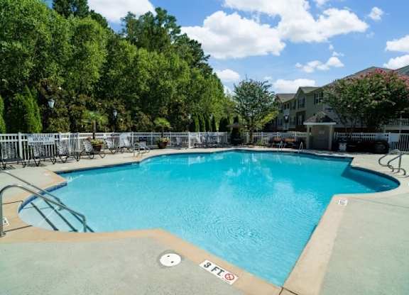 A large outdoor swimming pool surrounded by trees and a fence.