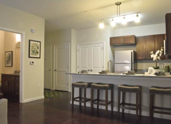 A kitchen with a refrigerator, sink, and bar stools.