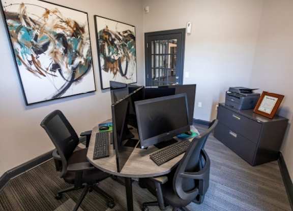 A modern office space with a round table, two chairs, and two computer monitors.