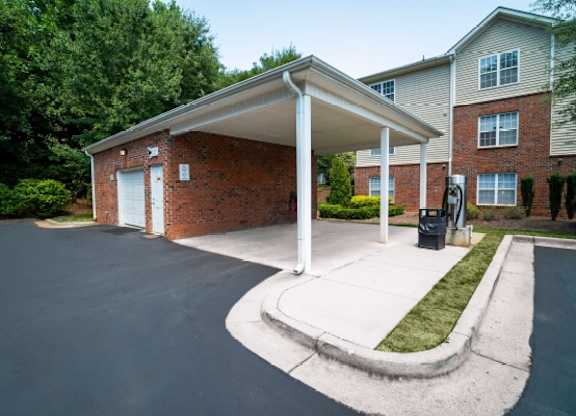 A covered parking area in front of a brick building.
