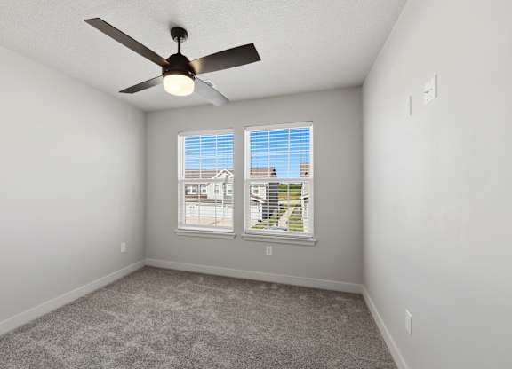 A room with a ceiling fan and a window showing a view of a residential area.
