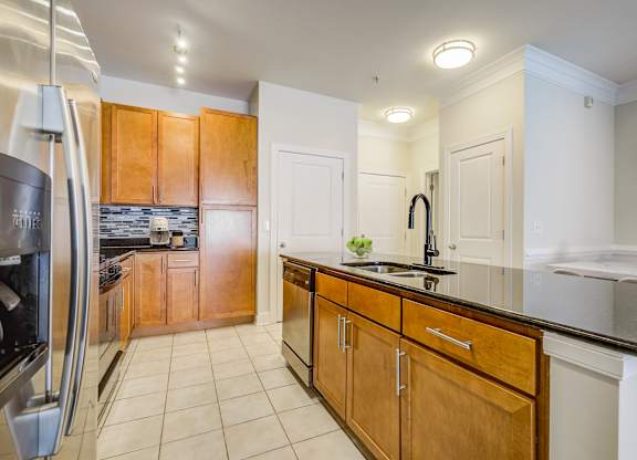 Apartments Near National Harbor - Tribeca at Camp Springs - A kitchen with wooden cabinets and a black countertop