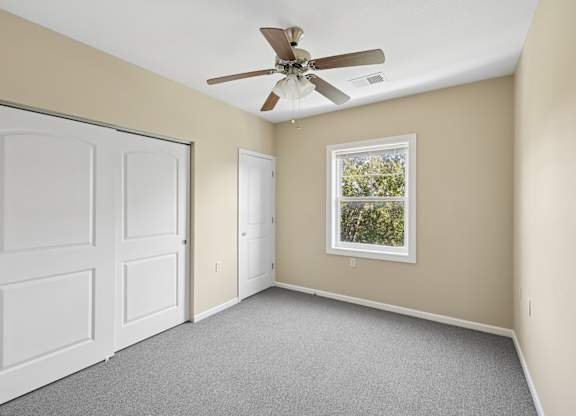 A room with a ceiling fan and a window showing trees outside.