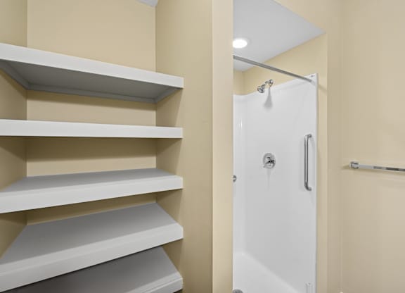 A white door is in a bathroom with a white shelving unit.
