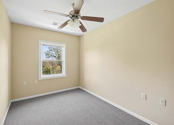 A room with a ceiling fan and a window showing trees outside.