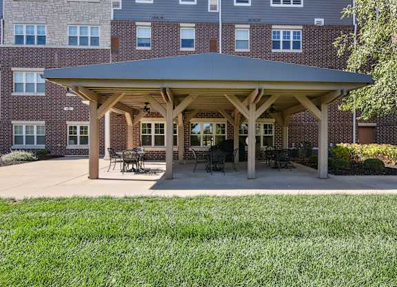 A covered patio area with tables and chairs in front of a brick building.