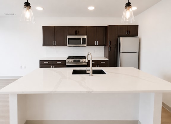 A modern kitchen with a white island and dark brown cabinets.