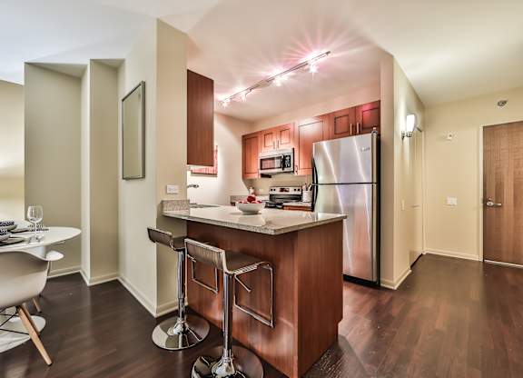 A kitchen with a refrigerator, microwave, and bar stools.