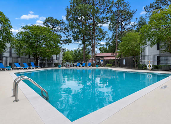 A swimming pool surrounded by trees and chairs.