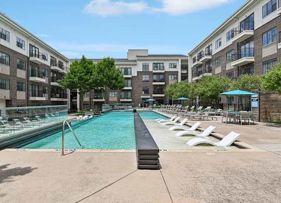 Markethaus 3700 A large swimming pool surrounded by lounge chairs and umbrellas in front of apartment buildings.