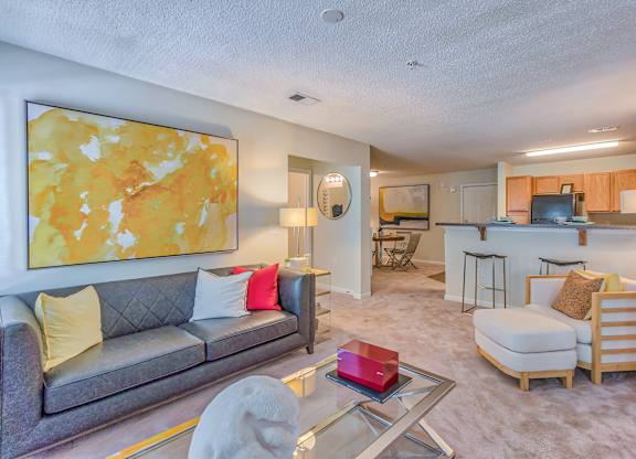 A living room with a grey couch and a yellow and orange painting on the wall.