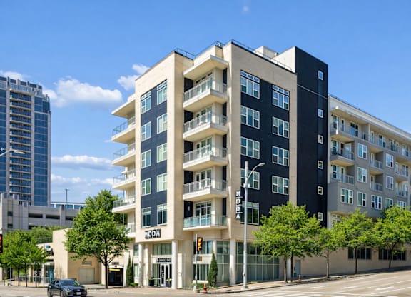 A modern apartment building with balconies and a car parked in front.
