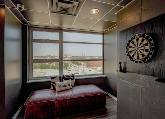 A dartboard hangs on a wall next to a window with a view of a cityscape.