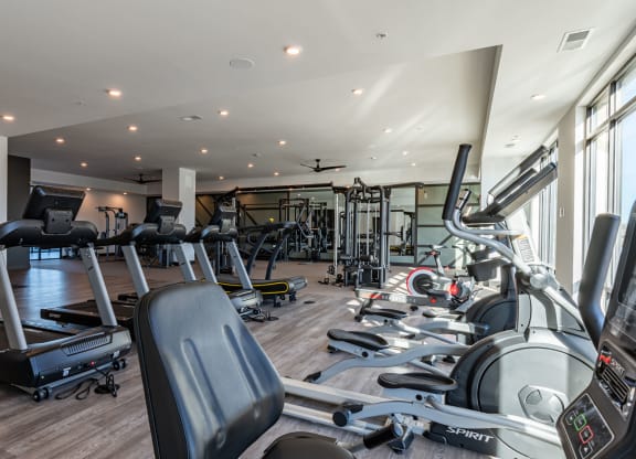 Carmel, IN, Apartments Near Palladium - North End - 24-Hour Fitness Center with Elliptical Machines, Stationary Bikes, Treadmills, Free Weights, Ceiling Fans, Mirror Wall, and Large Windows.