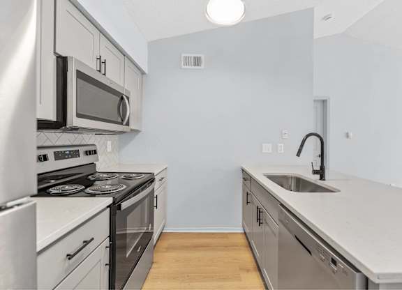 A modern kitchen with stainless steel appliances and a wooden floor.