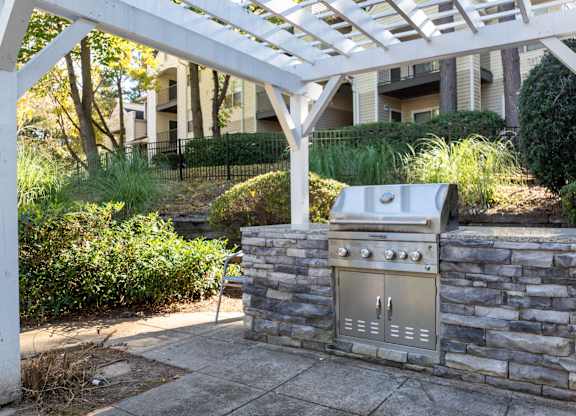 A BBQ grill is built into a stone wall under a white pergola.