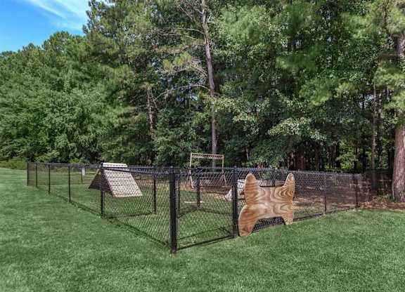 A dog house is behind a chain link fence in a grassy area.