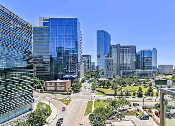 A cityscape with a mix of modern and older buildings, a clear blue sky, and a road with vehicles.