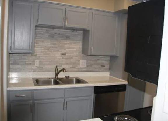 A kitchen with a black fridge and a stone backsplash.