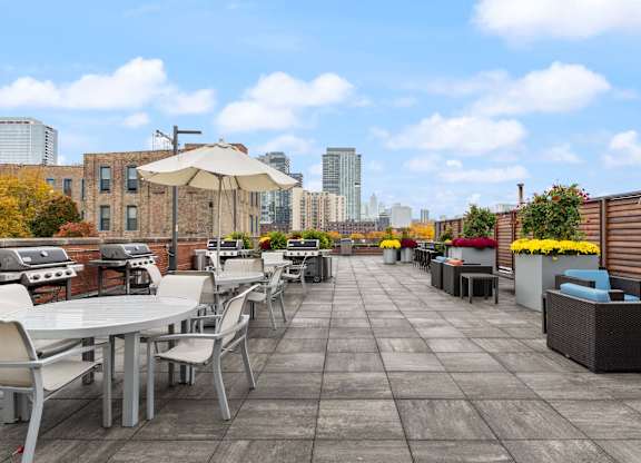 A rooftop patio with tables and chairs overlooking a city skyline.