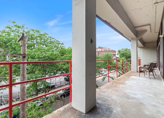 A balcony with a red railing and a view of a street below.
