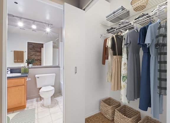 A white bathroom with a toilet and a white closet with clothes hanging.