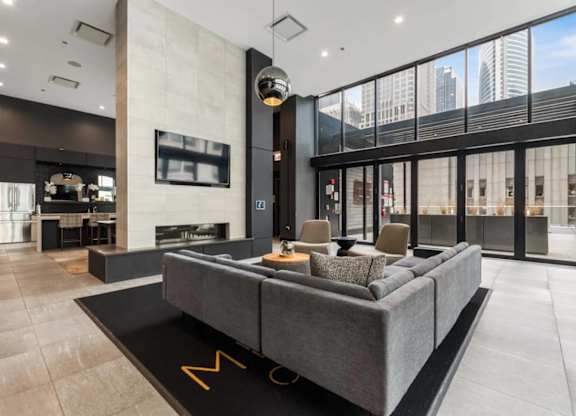 A modern living room with a grey sofa and a large window overlooking the city.