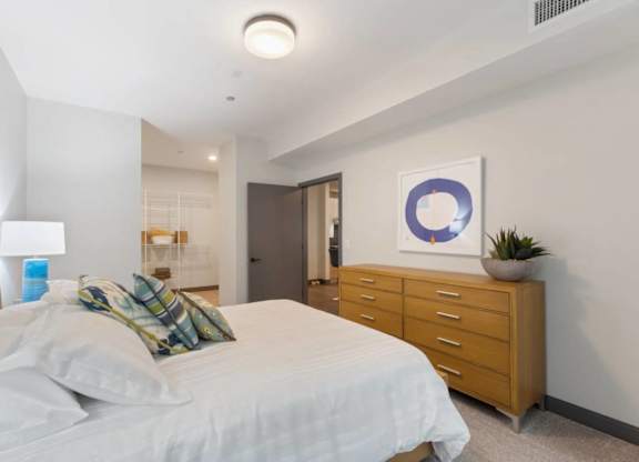 A bedroom with a bed, nightstand, and a plant.