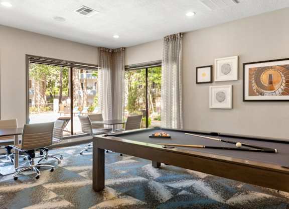 A pool table is in the middle of a room with a view of trees outside the window.