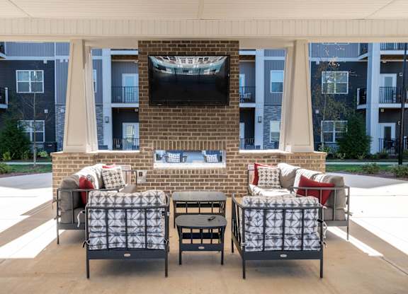 A patio with a couch, chair, and a television on a brick wall.