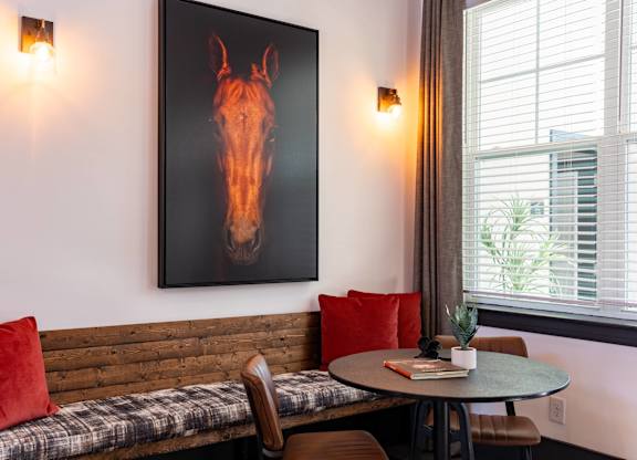 A painting of a horse head is on the wall above a bench with a table and chairs.